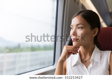 Asian woman traveler contemplating outdoor view from window of train. Young lady on commute travel to work sitting in bus or train.