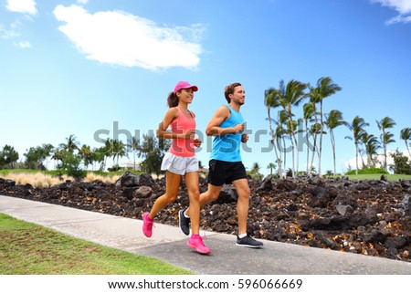 Happy couple of runner friends running training for marathon race together in summer jogging on street sidewalk neighborhood park.
