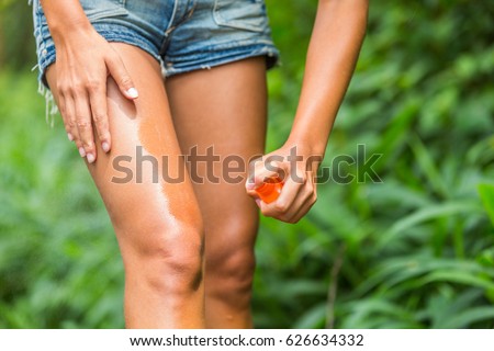 Mosquito repellent spray. Woman spraying insect repellent against bug bites, zika virus etc on legs skin outdoor in nature forest using spray bottle.