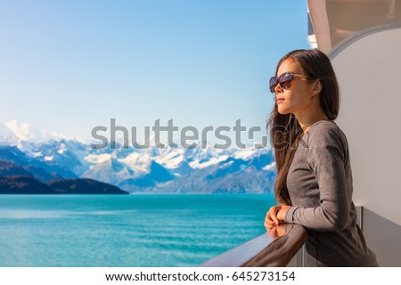 Luxury travel Alaska cruise vacation woman relaxing on balcony enjoying view of mountains and nature landscape. Asian girl sunglasses tourist.