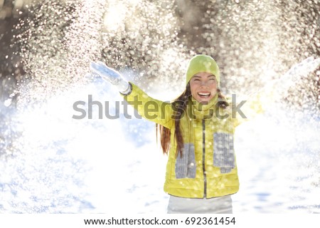 Happy winter fun woman playing throwing snow with arms up open in freedom enjoying the cold season