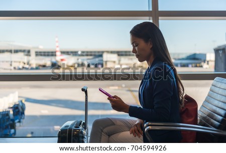 Airport phone travel woman using mobile phone in business class lounge waiting for plane flight texting sms message on smartphone. Technology and travel people frequent flying lifestyle.