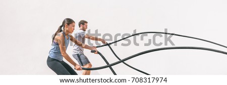 Gym fitness sport fit couple working out battle rope exercise banner panorama. Woman and man cross training arms muscles and cardio with battling rope. Core workout panoramic crop.