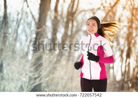 Winter run woman runner exercising in outdoor forest park. Asian athlete girl training cardio during cold season wearing gloves, warm headband for protecting the ears and jacket.