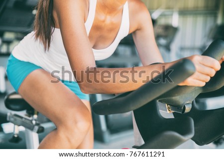 Indoor cycling woman doing HIIT cardio workout biking on indoors gym bike. Girl cyclist working out interval training on bicycle. Closeup of legs and thighs for fat weight loss.
