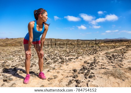Trail runner woman tired breathing hard during ultra running cardio exercise exhausted on difficult run race. Asian young athlete in desert summer heat training hard.