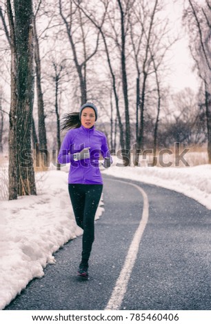Winter run cold training outdoor. Asian runner girl doing running exercise in snow. Fit woman healthy active jogging during snowstorm with falling snow and ice on city street. Young people lifestyle.
