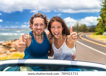 Car happy road trip young drivers driving in convertible cabriolet car. Smiling couple doing thumbs up on summer holiday road trip in new car. Interracial happy couple.