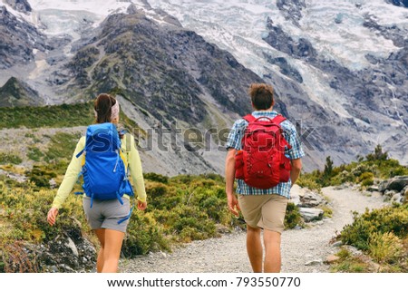 Hiking people walking on mountain trail trekking with backpacks. Hikers couple backpacking in nature, outdoor active lifestyle. Two young adults from behind.