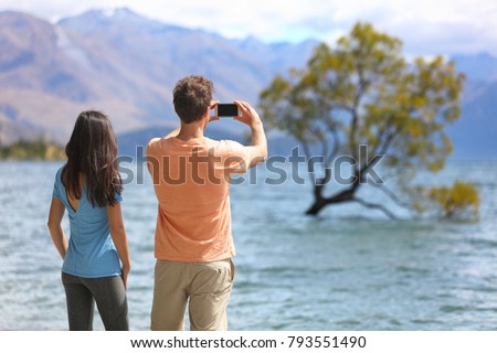 New Zealand tourists taking phone pictures of Wanaka Lone Tree at lake. People looking at view of famous touristic attraction in south island, Otago Region, NZ.