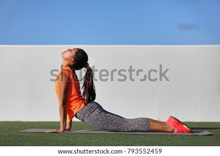 Fitness yoga woman stretching practicing morning sequence doing cobra pose or upward facing dog, bhujangasana. Fit fitness girl stretching summer park grass. Beautiful multiracial female model.