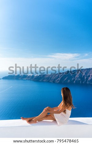 Luxury travel vacation Europe tourist woman relaxing at fancy hotel resort balcony in greek Santorini island, Greece with view over the Mediterranean Sea and Oia. Elegant girl living jetset lifestyle.