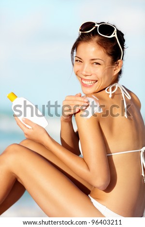 Sunscreen woman. Girl putting sun block on beach holding white sun tan lotion bottle. Beautiful young woman enjoying sunshine on summer vacation. Mixed race Asian / Caucasian female bikini model