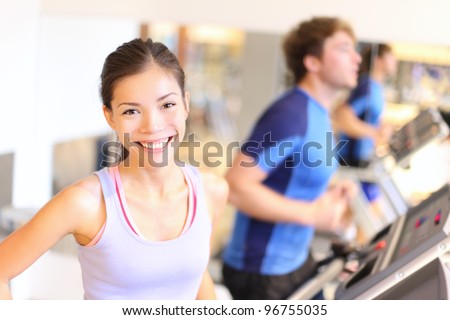 Fitness people portrait in gym. Woman smiling happy during running workout on treadmill in fitness center. Mixed race Cauasian / Chinese Asian female fitness model.