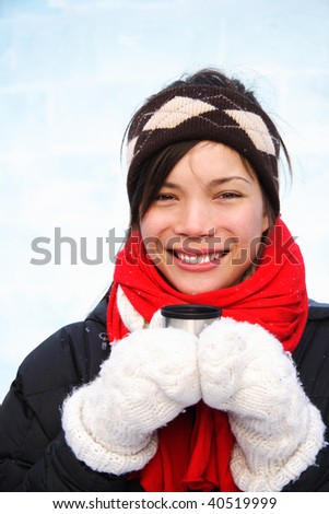 Woman drinking hot coffee or tea outdoors in winter. Mixed ethnic asian / caucasian model. The background is an ice wall.