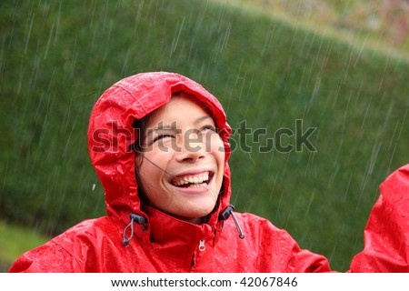 Young woman wearing a red raincoat enjoying the rain and having fun outside.