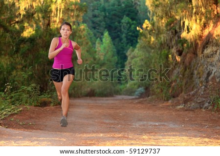 Female athlete running on forest road - copy space. Chinese Asian / Caucasian female woman runner.