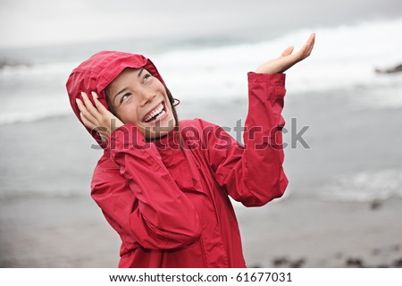 Woman in red raincoat enjoying the rain and having fun outside on the beach on a gray rainy autumn day. Asian / Caucasian model.