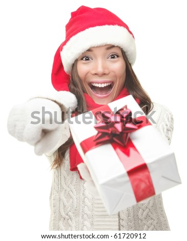 Christmas woman holding / giving gift excited pointing. Happy smiling woman in santa hat giving you a present being joyful, fresh and cheerful. Asian / Caucasian model isolated on white background.