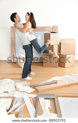 Couple moving in happy and excited in new home. Young interracial couple with moving boxes and furniture assembly in new house or apartment. Caucasian man and Asian woman embracing.