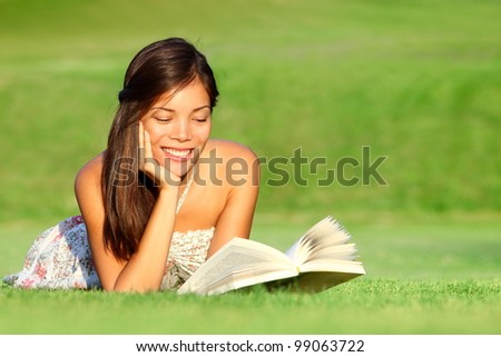 Reading. Woman reading book in park during spring / summer time. Happy smiling beautiful young university student studying lying down in grass. Mixed race Asian Chinese Caucasian female model outdoors