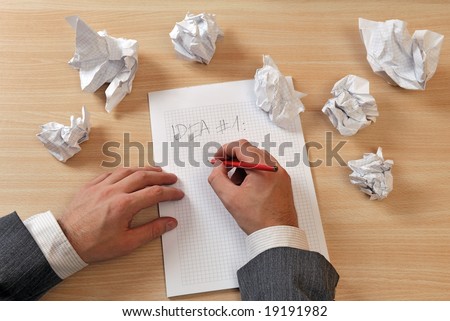 A man in business suite is writing ideas on a paper, with few papers crumpled and discarded