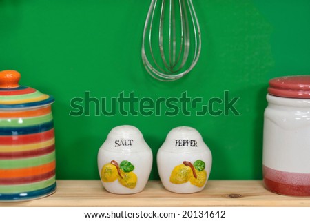 Handmade salt and pepper containers in front of a green wall with few other kitchen items out of focus