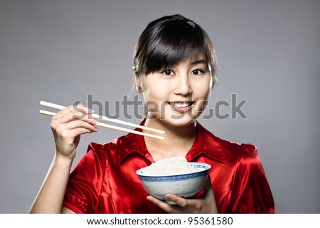 A young Asian girl eating rice with bowl and chopsticks
