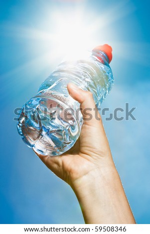 A hand holding a bottle of mineral water into the sun on a blue sky background - intentional flare.