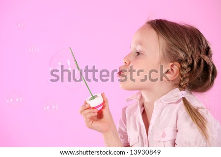 Little girl blowing soap sud. Studio shot on pink background.