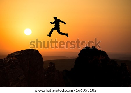 silhouette of a man jumping off a cliff in the direction of the bright sun