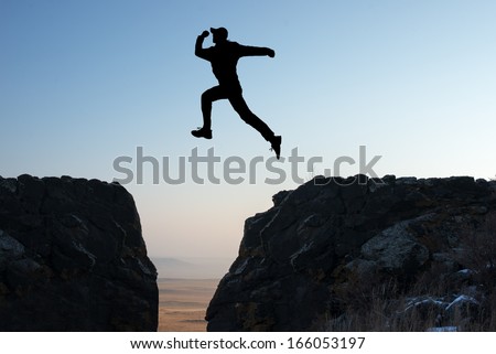 silhouette of a man jumping off a cliff in the direction of the morning