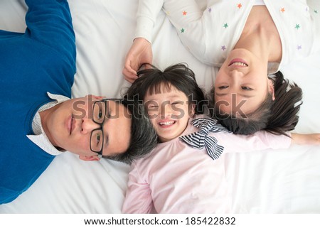 Happy family, young parents and daughter lying in bed.