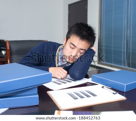 Young business man sleeping in front of the desk, the performance of work pressure