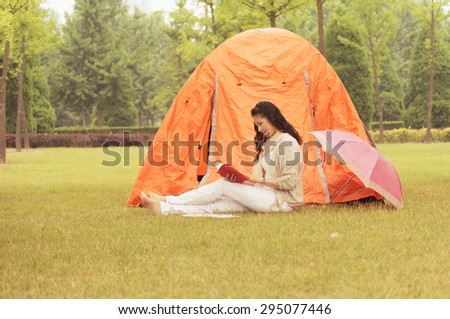 Old woman reading a book. Next to a tent on the lawn