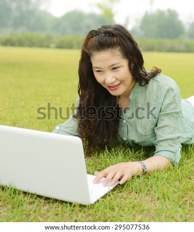 Old woman lie on the grass using laptops