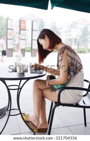 woman working with her phone and laptop in a restaurant terrace with a cup of coffee