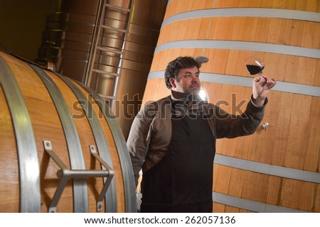 Winemaker tasting wine amongst oak casks.