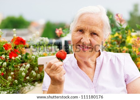Elderly smiling woman sitting on the terrace, holding a strawberry