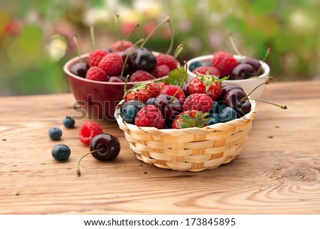 Berries in bowls on wooden table in a garden, fruits, cherry, raspberry, strawberry and blueberry
