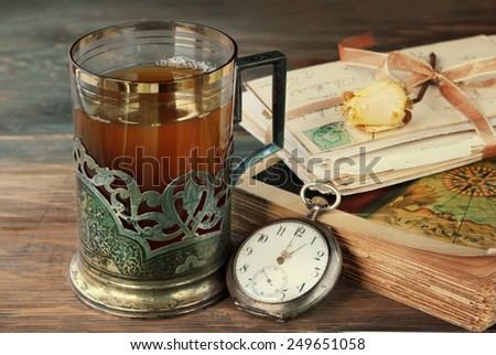 Tea in vintage glass-holder old book, letters  and watch on wooden table. retro filtered image
