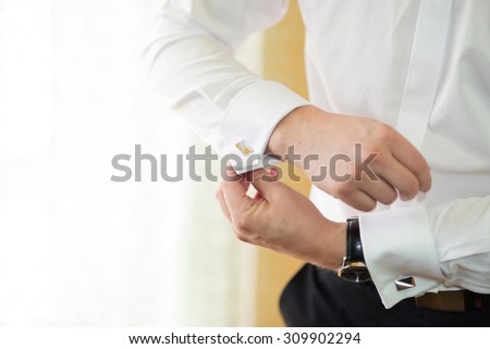 groom putting on cuff-links as he gets dressed in formal wear close up, close up of a hand man how wears white shirt and cufflink