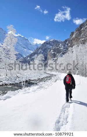 Lone hiker on river trail in snow covered alpine valley.