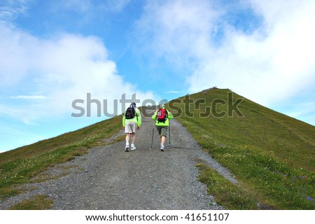 Couple of senior hikers with backpacks climbing up a mountain path.