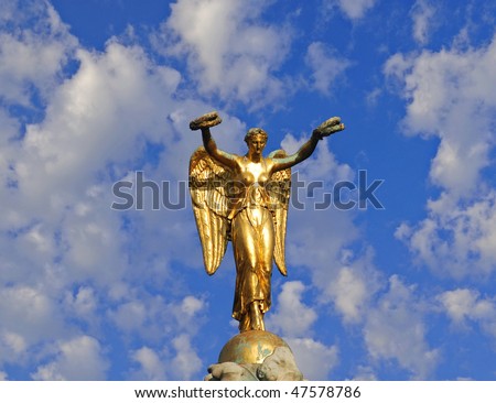 Statue of Golden Angel at the top of a column in Paris against a cloud strewn blue summer sky..