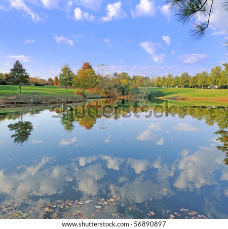 Small pond in Fall with sky and trees reflected on its surface.