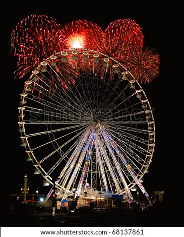 Night photo of brightly lit Ferris wheel with red fireworks exploding in the background.