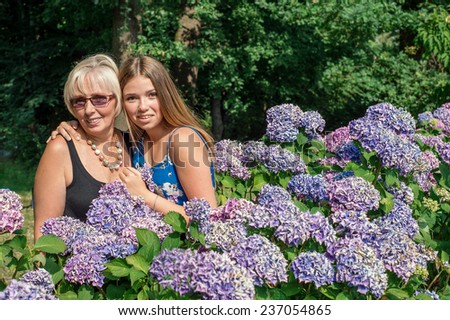 Two women of different generations standing near flowers hydrangeas. Mother and daughter. Grandmother and granddaughter.