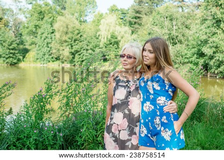 Two women of different generations are near a pond in the summer. Mother and daughter hugging. Grandmother and granddaughter.