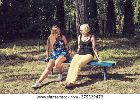 Two women of different generations sitting on a bench and talking. Mother and daughter. Grandmother and granddaughter.